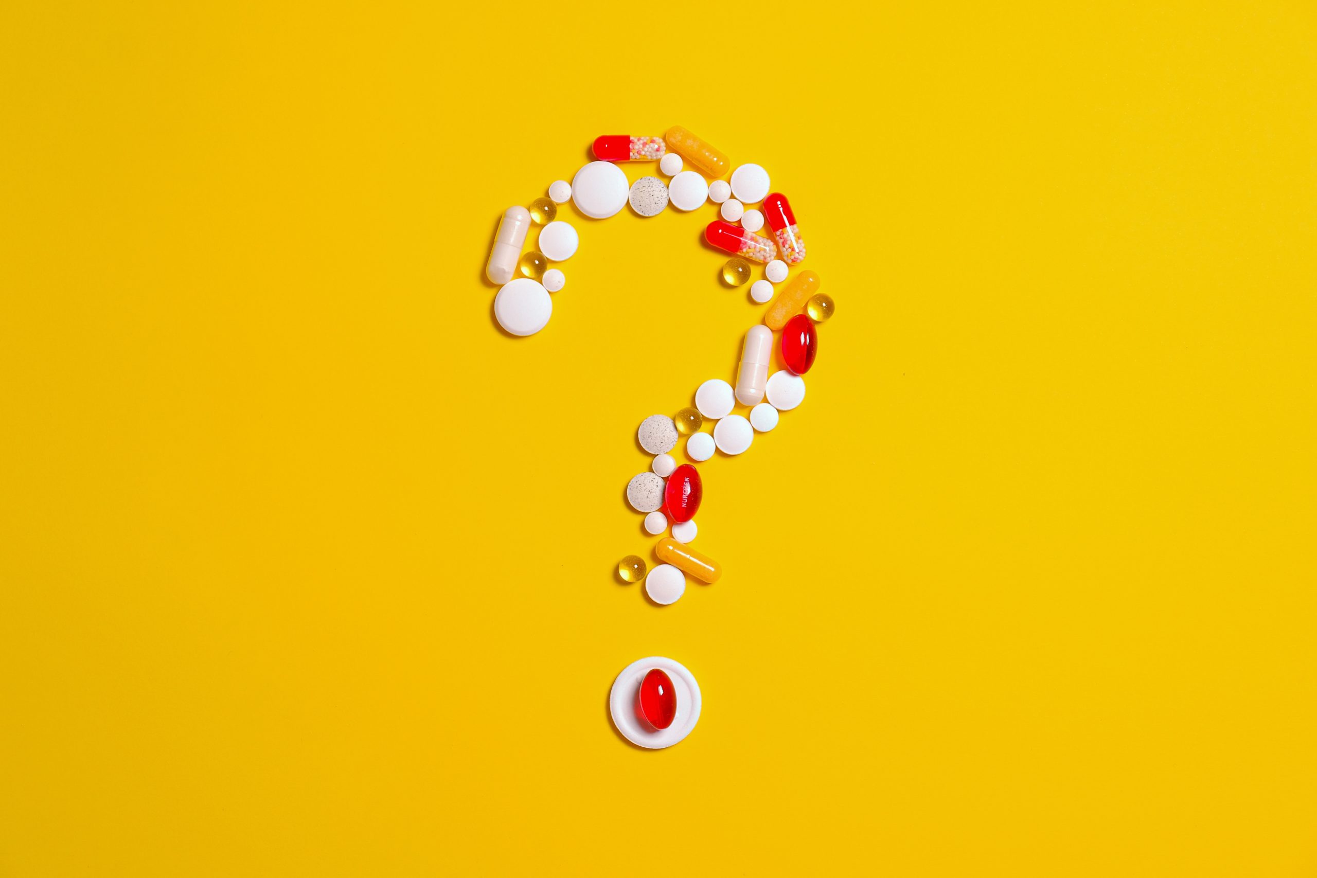 Pills and capsules arranged in the shape of a question mark on a yellow background